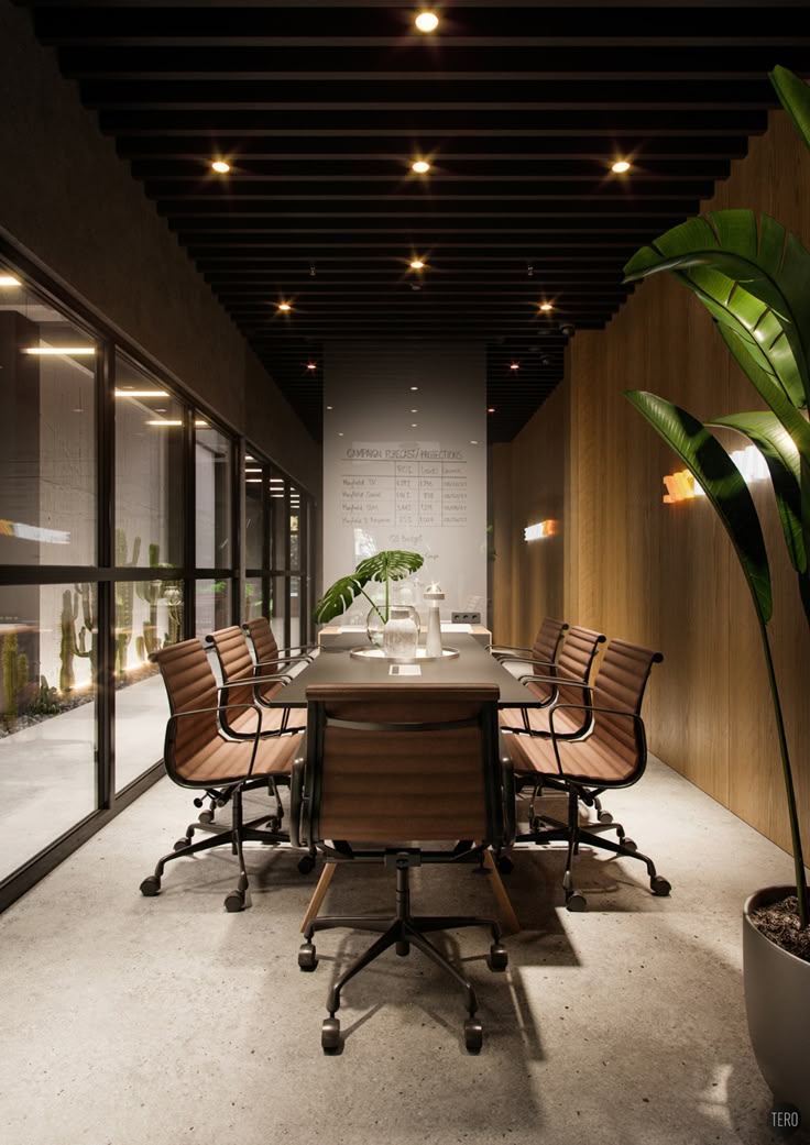 Long, narrow meeting room with a black slatted ceiling, warm wooden walls, glass wall overlooking a cactus garden, and brown leather office chairs around a black table with green plants.