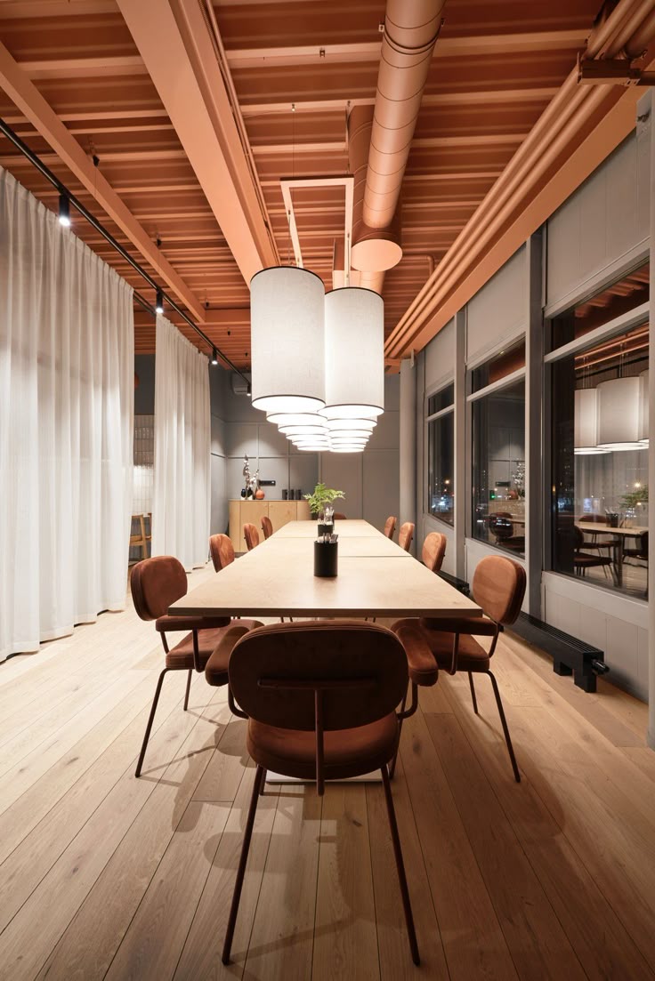 Warm-toned meeting room with terracotta-painted exposed ceiling, soft velvet chairs around a long wooden table, oversized pendant lights, and sheer white curtains.